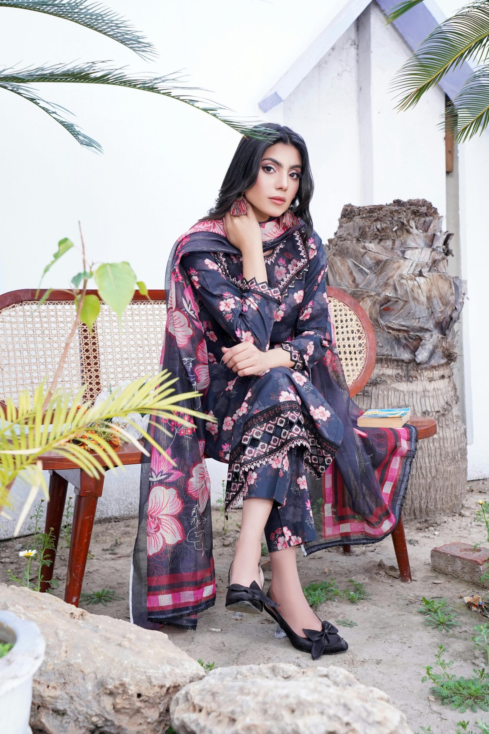 A fashionable model poses in a floral shalwar kameez in an outdoor setting.